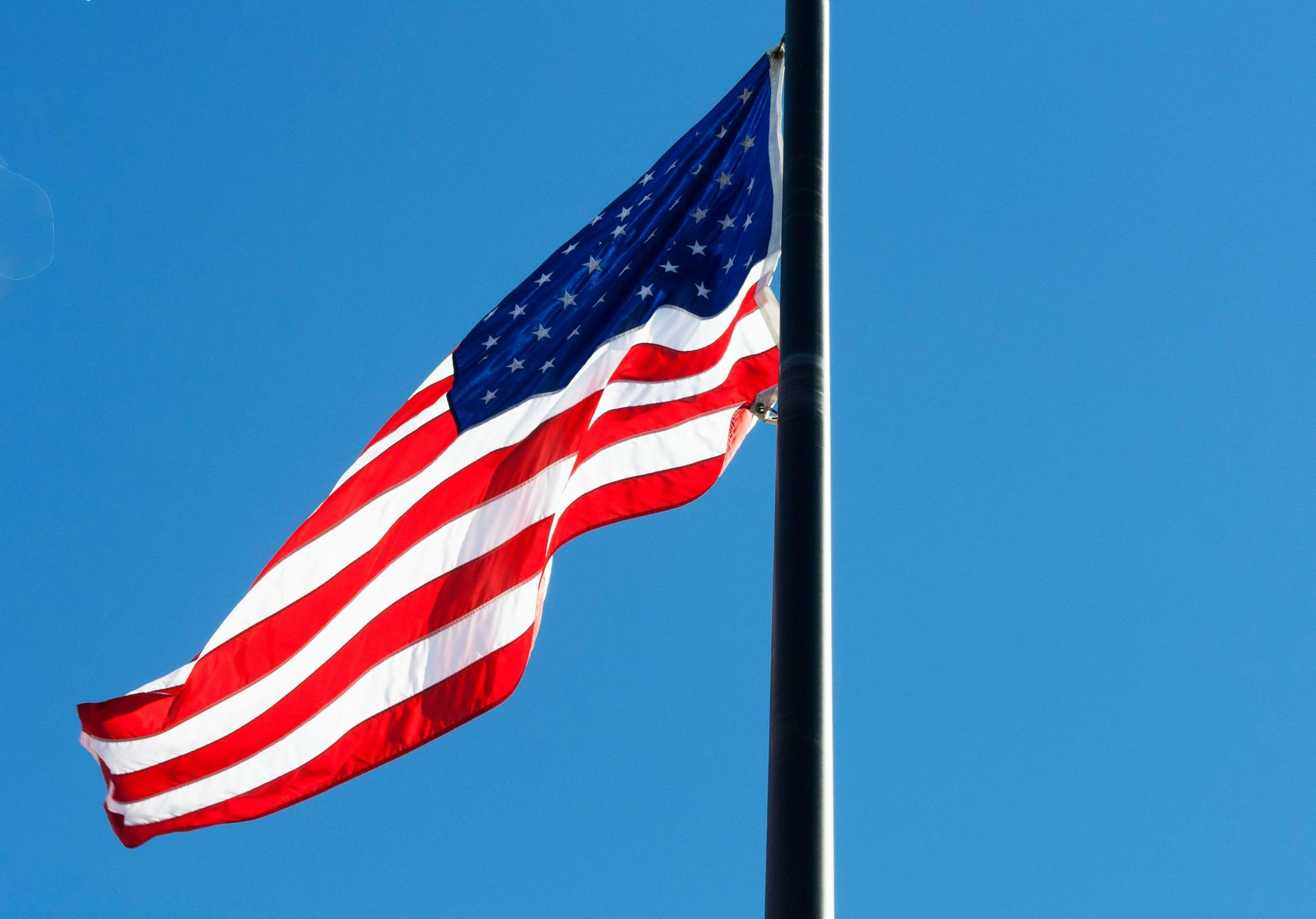 An american flag is waving in the wind against a blue sky