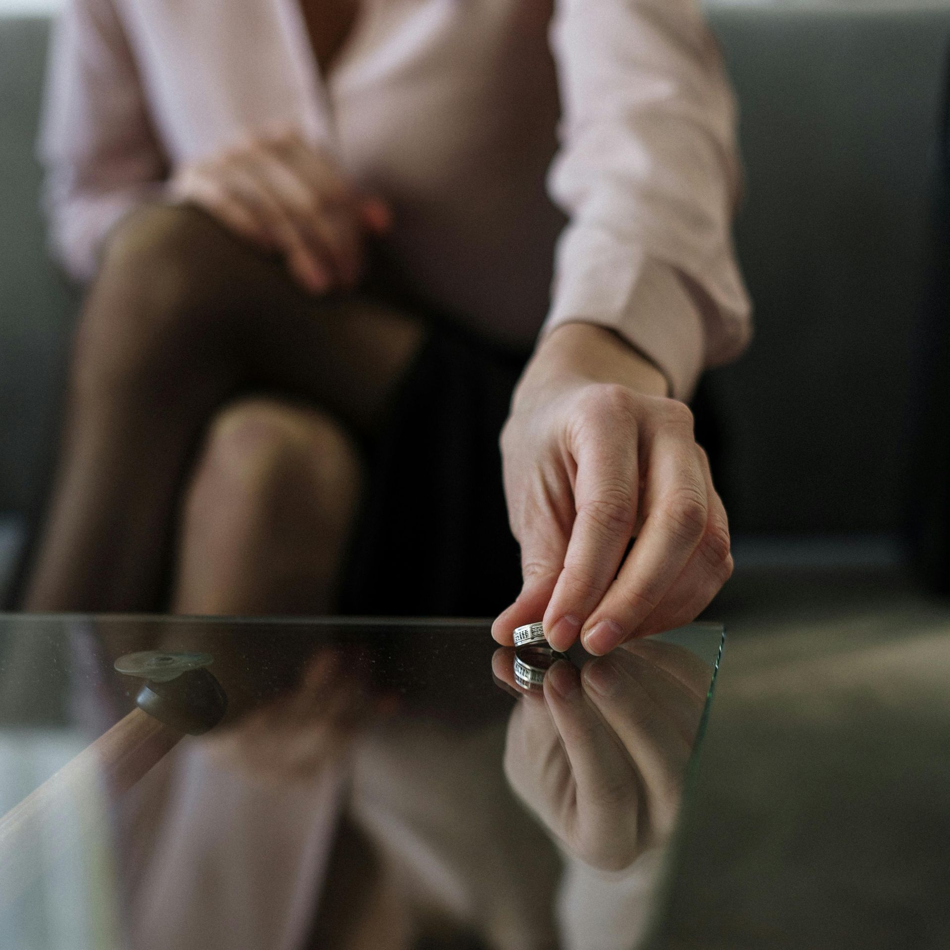 A woman is putting a wedding ring on a glass table.