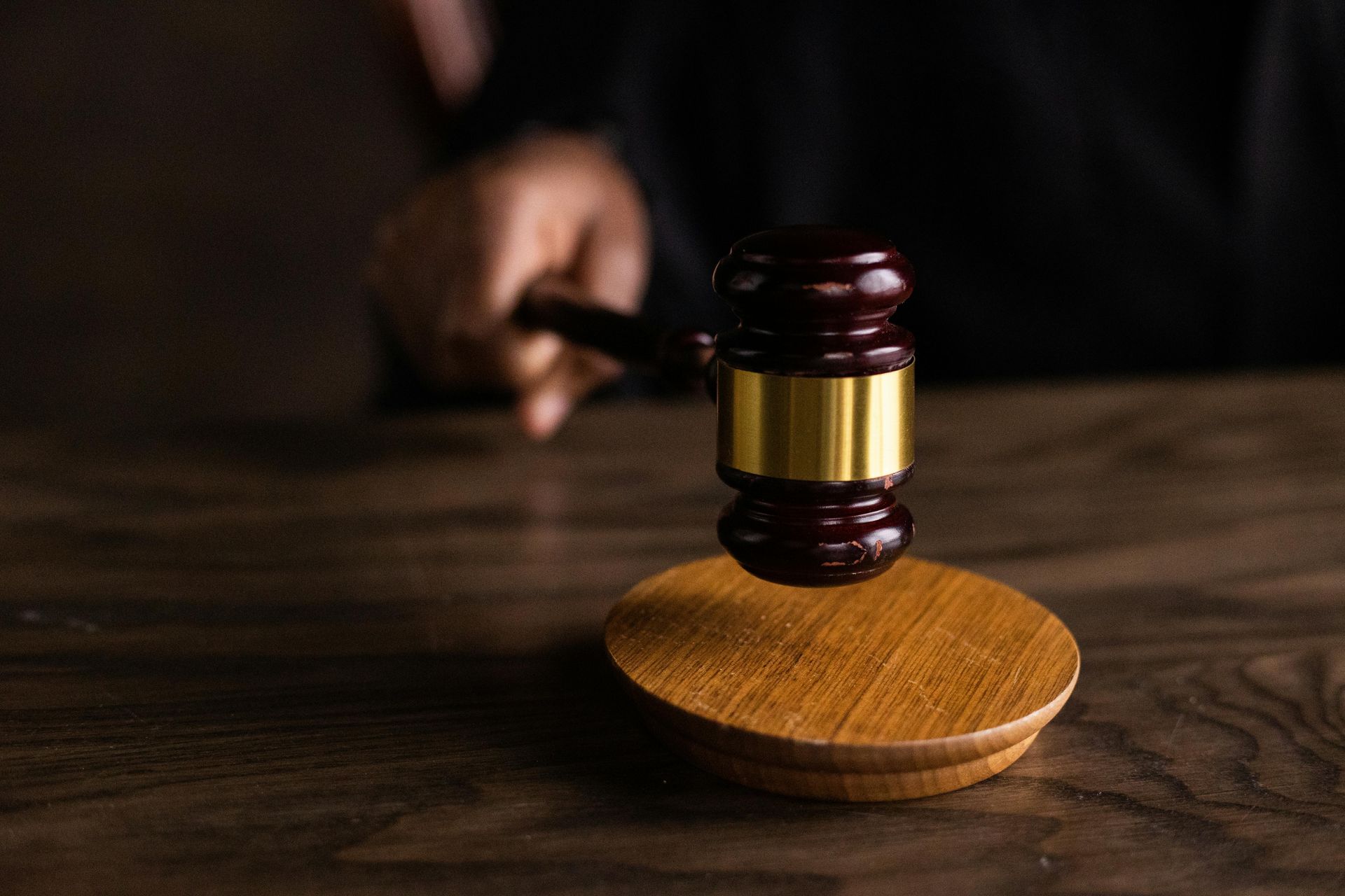 A person is holding a wooden gavel on a wooden table.