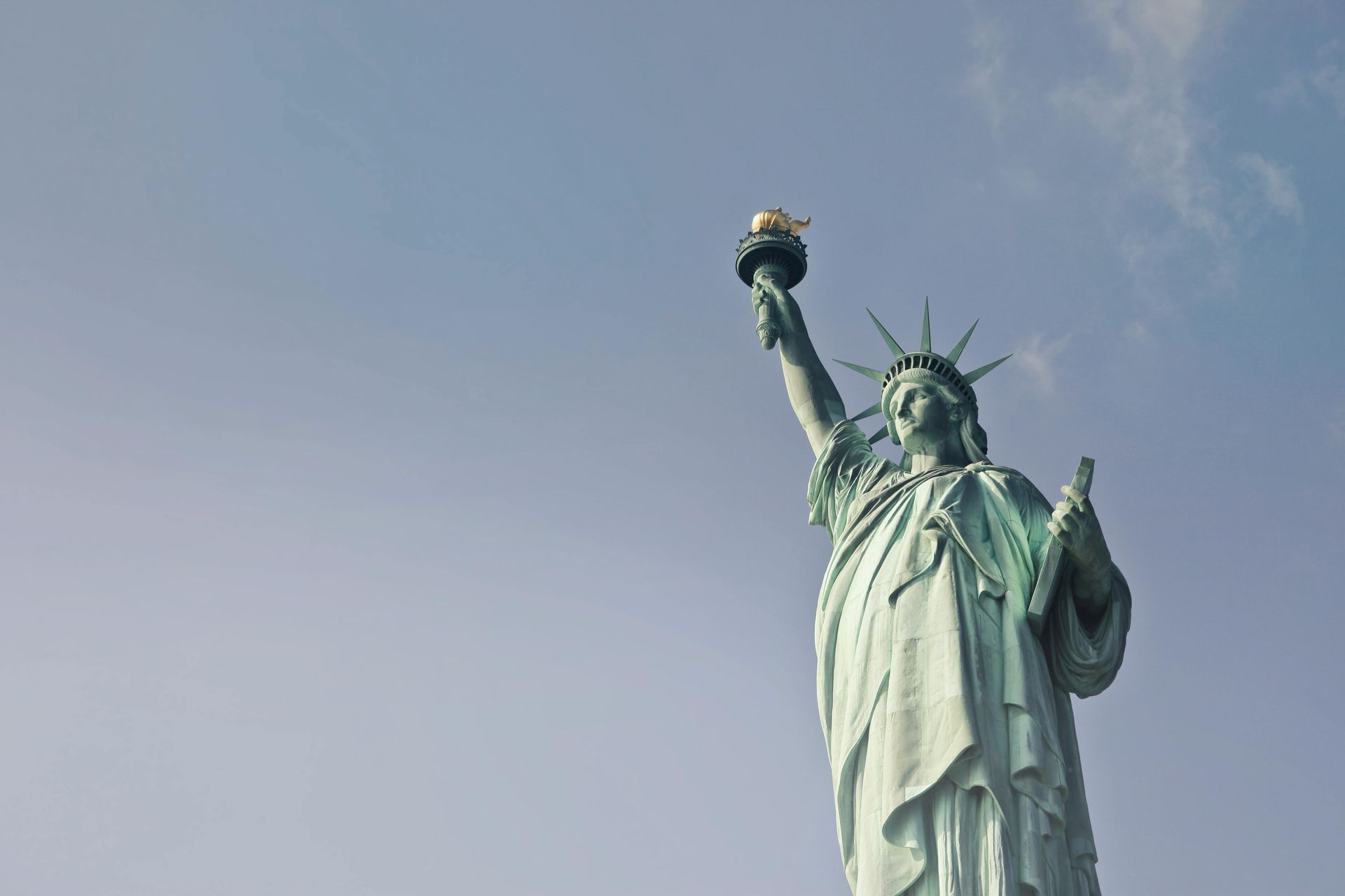 The statue of liberty is holding a torch in front of a blue sky.