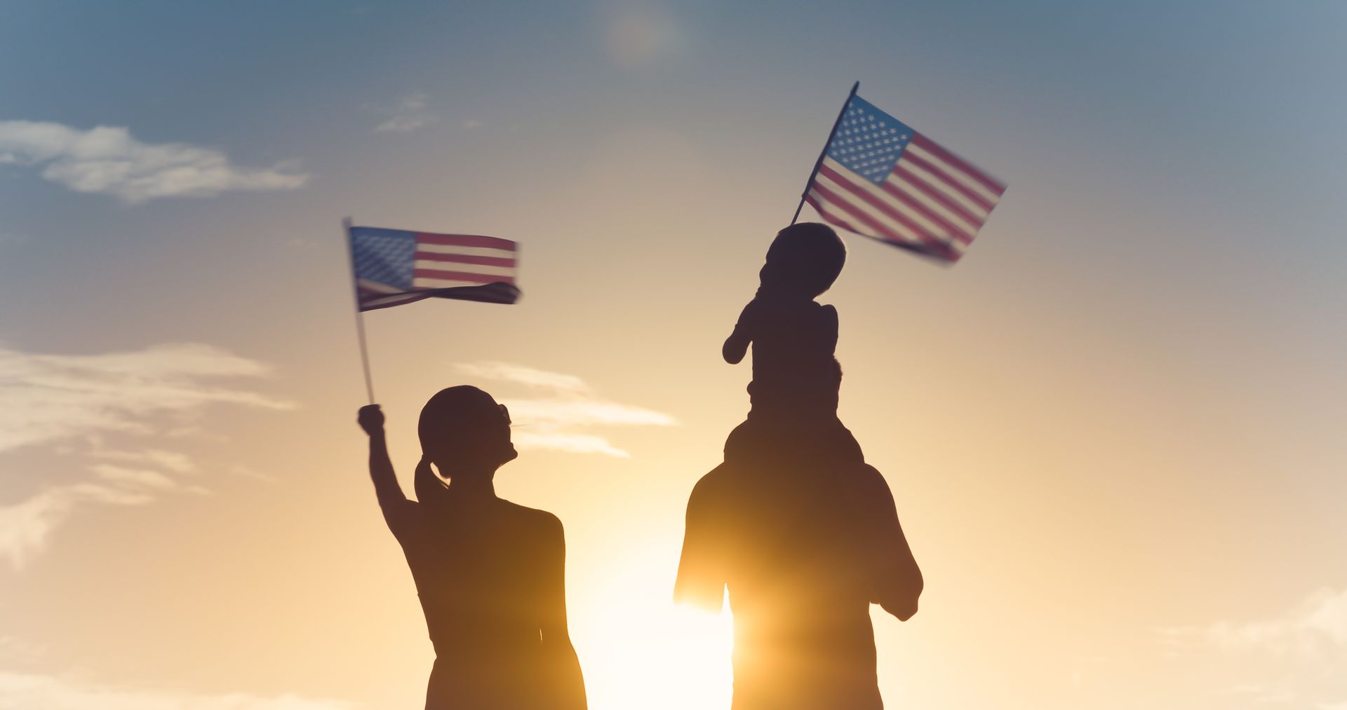 A woman and a child are holding american flags on their shoulders.