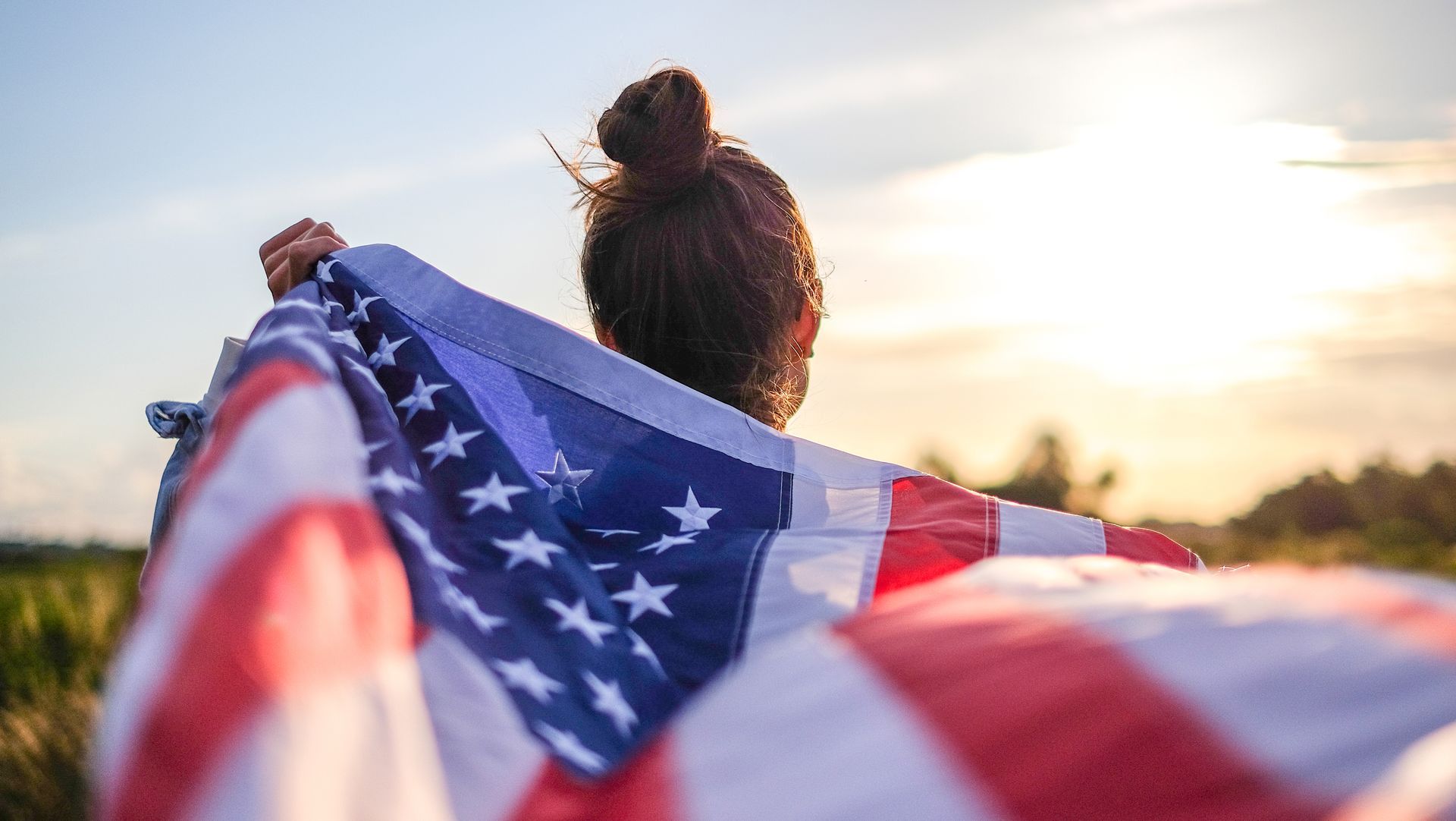 A woman is holding an american flag in a field.