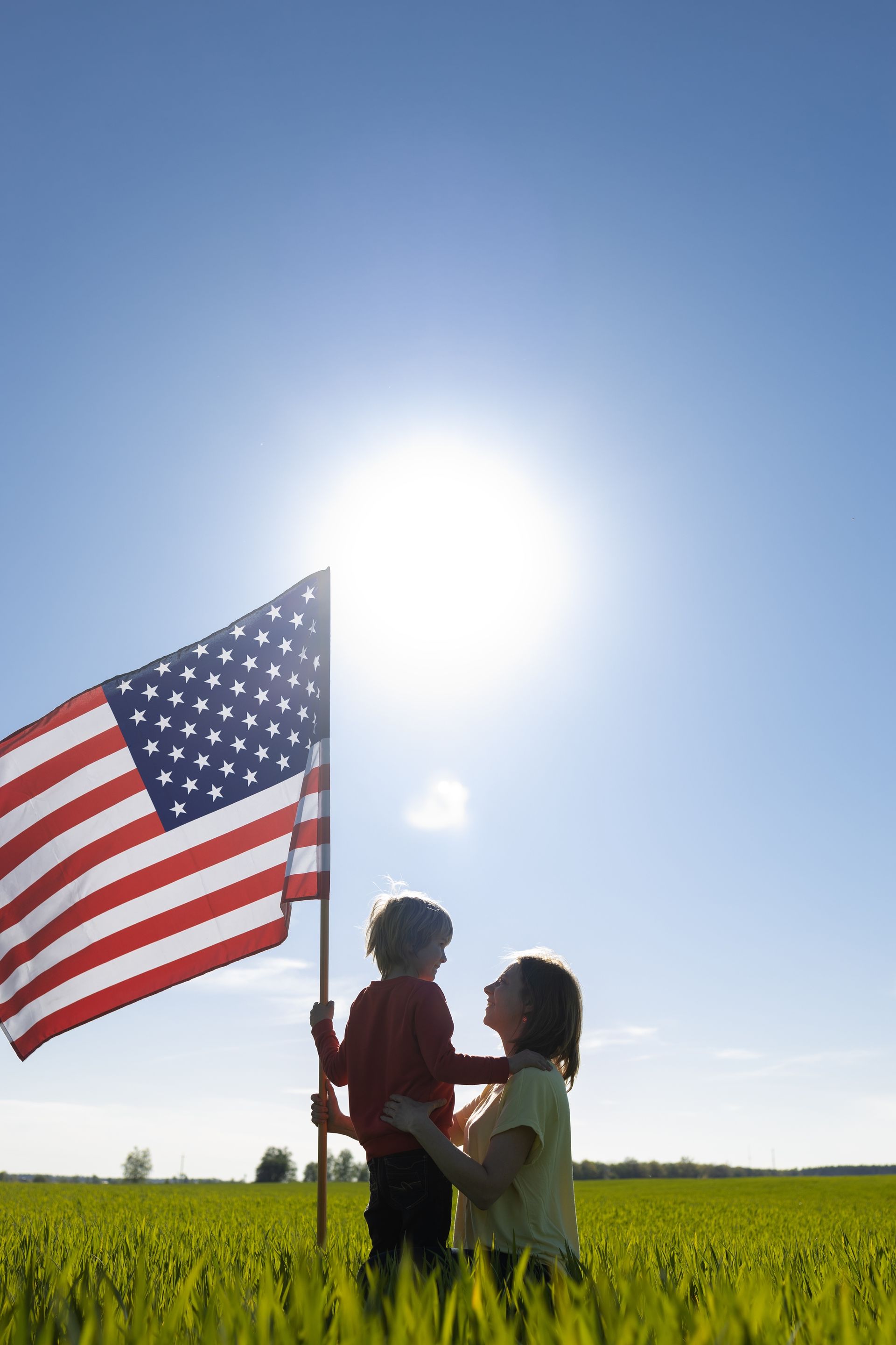 A woman and child are holding an american flag in a field.