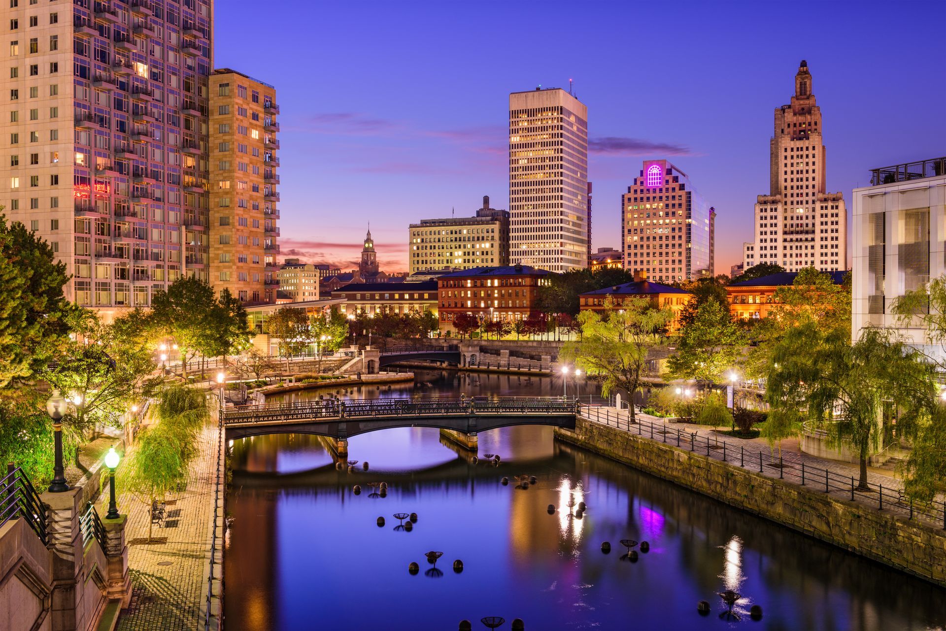 A city skyline at night with a river in the foreground.