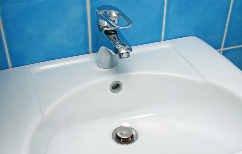 White bathroom sink with chrome faucet against blue tiled wall.