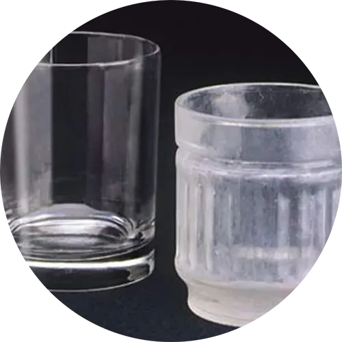 Two clear glass cups on a dark surface. The cup on the right has vertical ridges.
