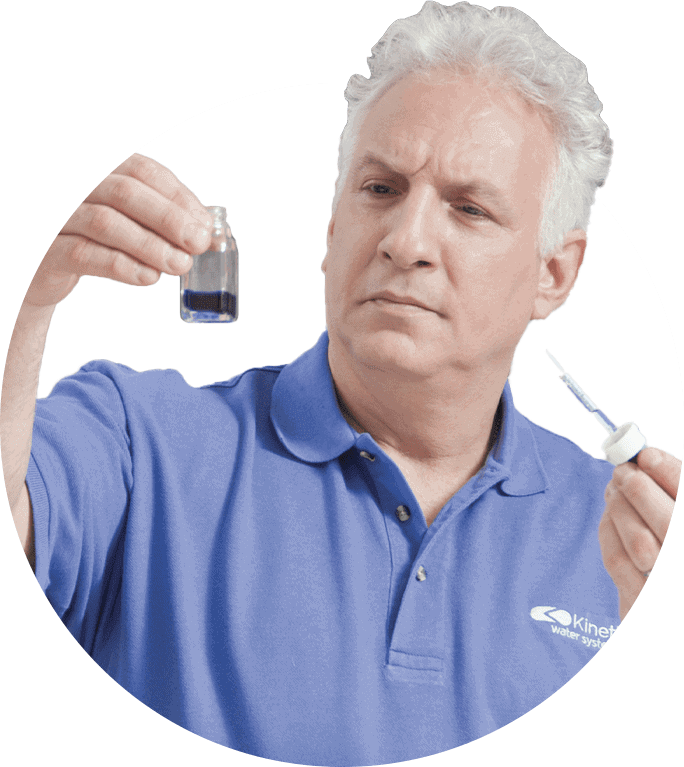 Man in blue shirt examining a dark liquid sample in a vial, using a dropper, with a concerned expression.