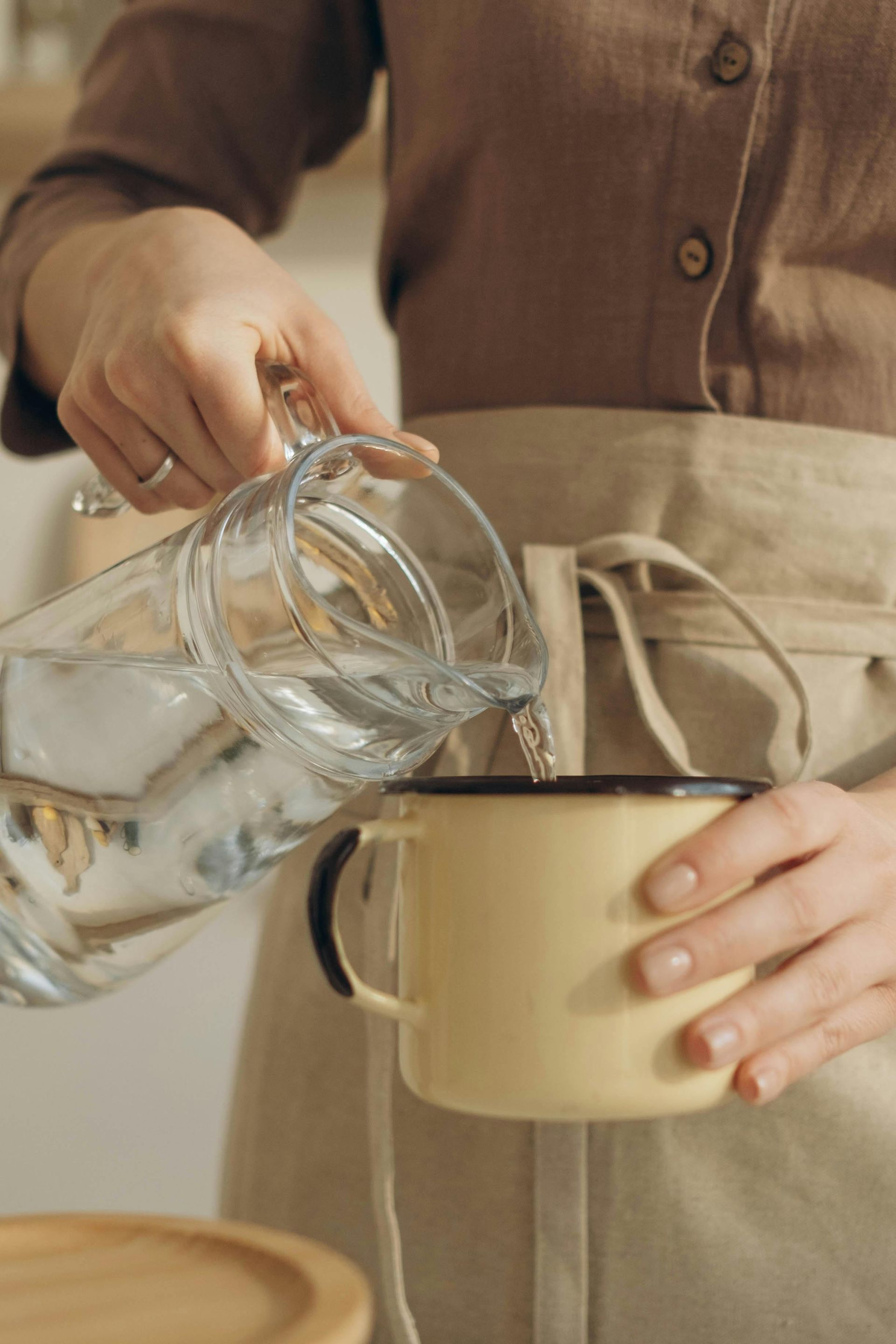 Woman pouring water from a glass pitcher into a yellow mug.