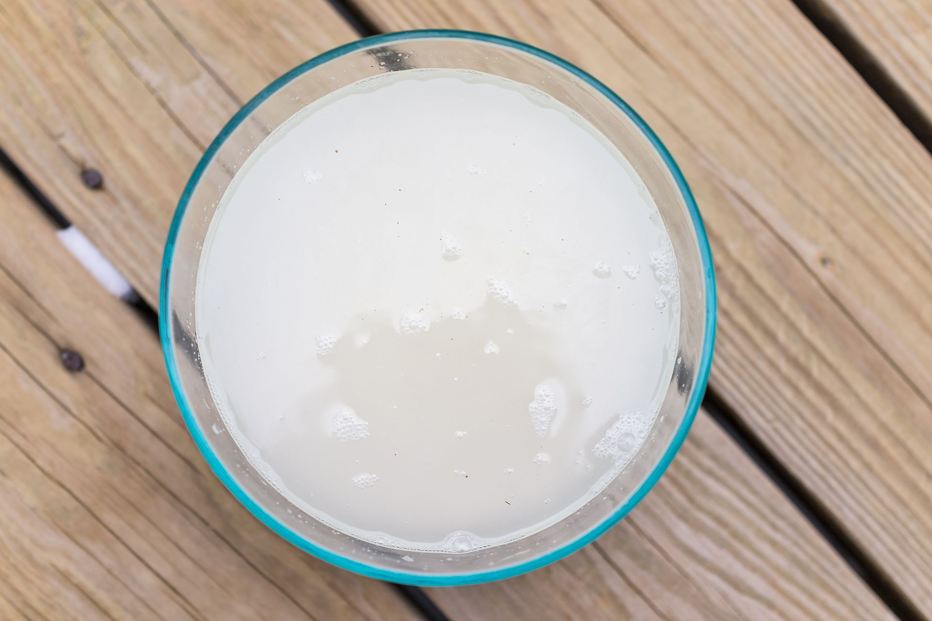 A clear, frosty margarita in a turquoise-rimmed glass on a wooden surface.