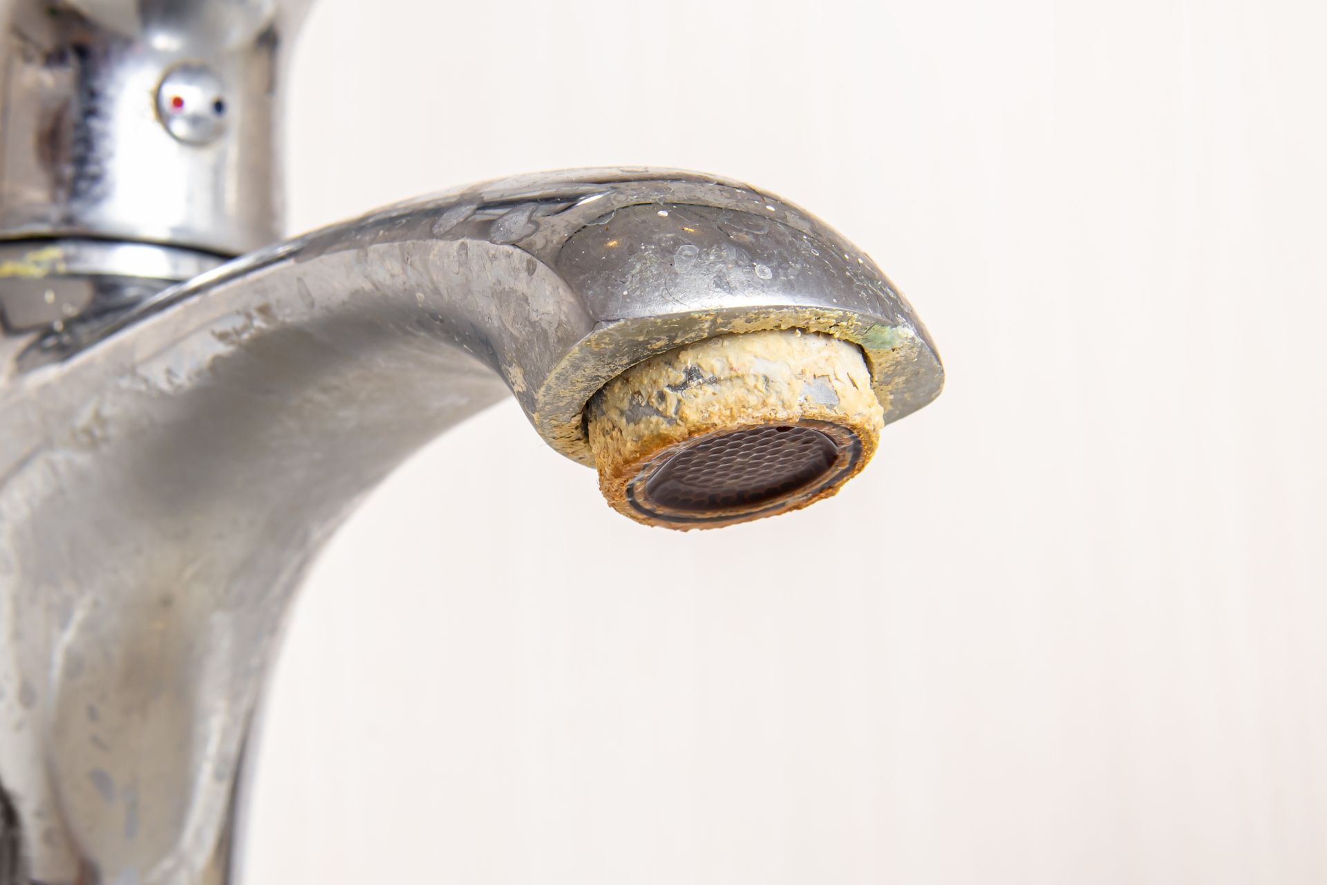 Close-up of a chrome faucet with a rusty, clogged aerator, likely due to hard water.
