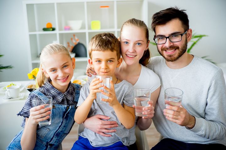 Family of four smiling, holding glasses of water indoors.