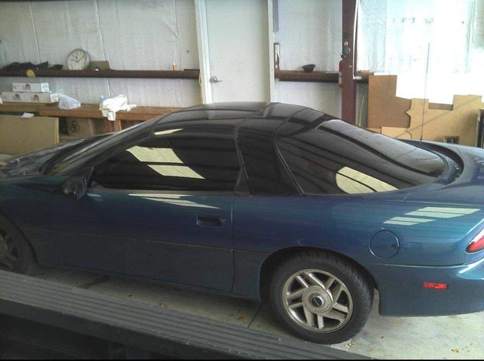 A blue car with a black roof is parked in a garage