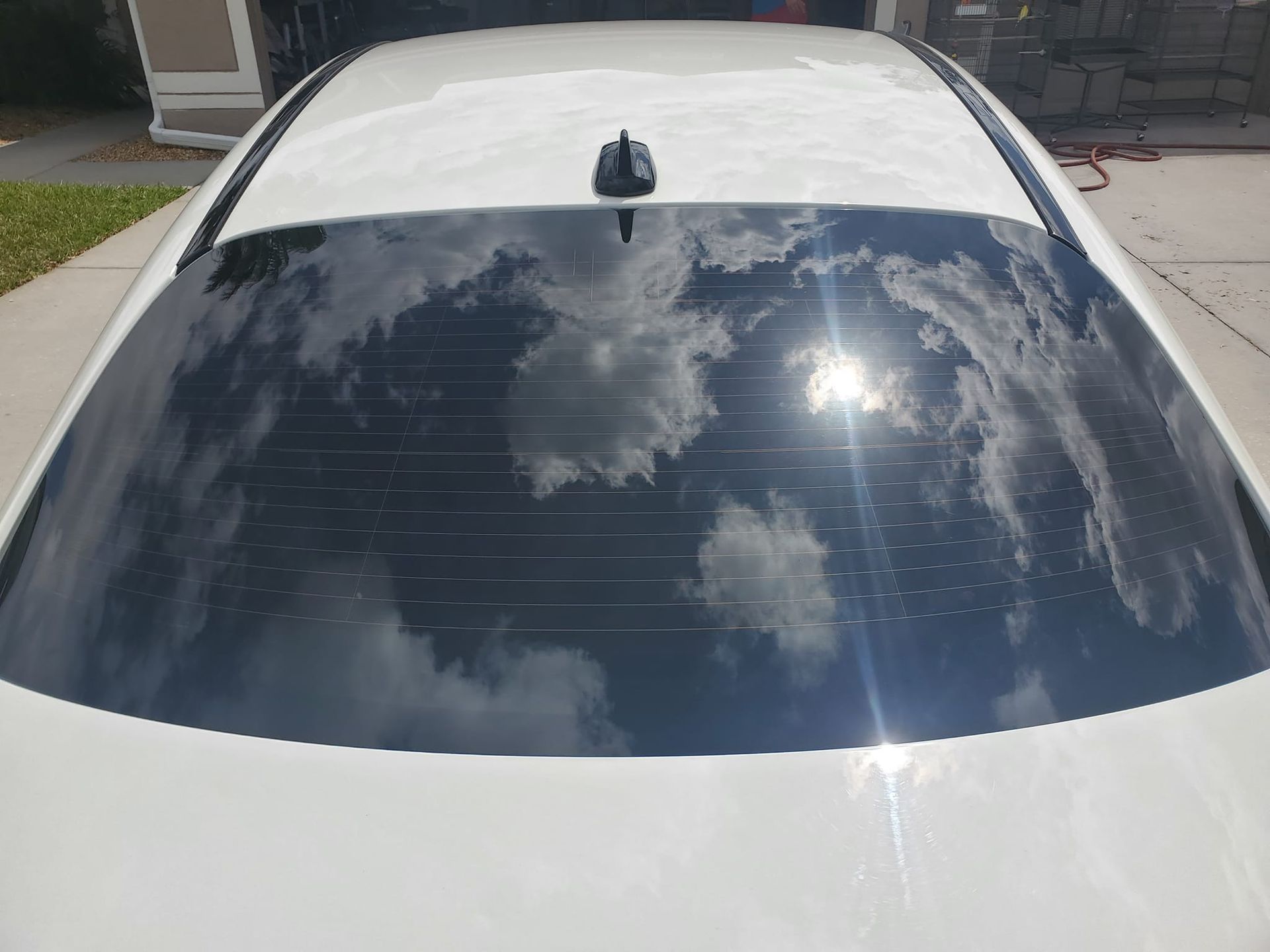 A white car with a black antenna is parked in a driveway.