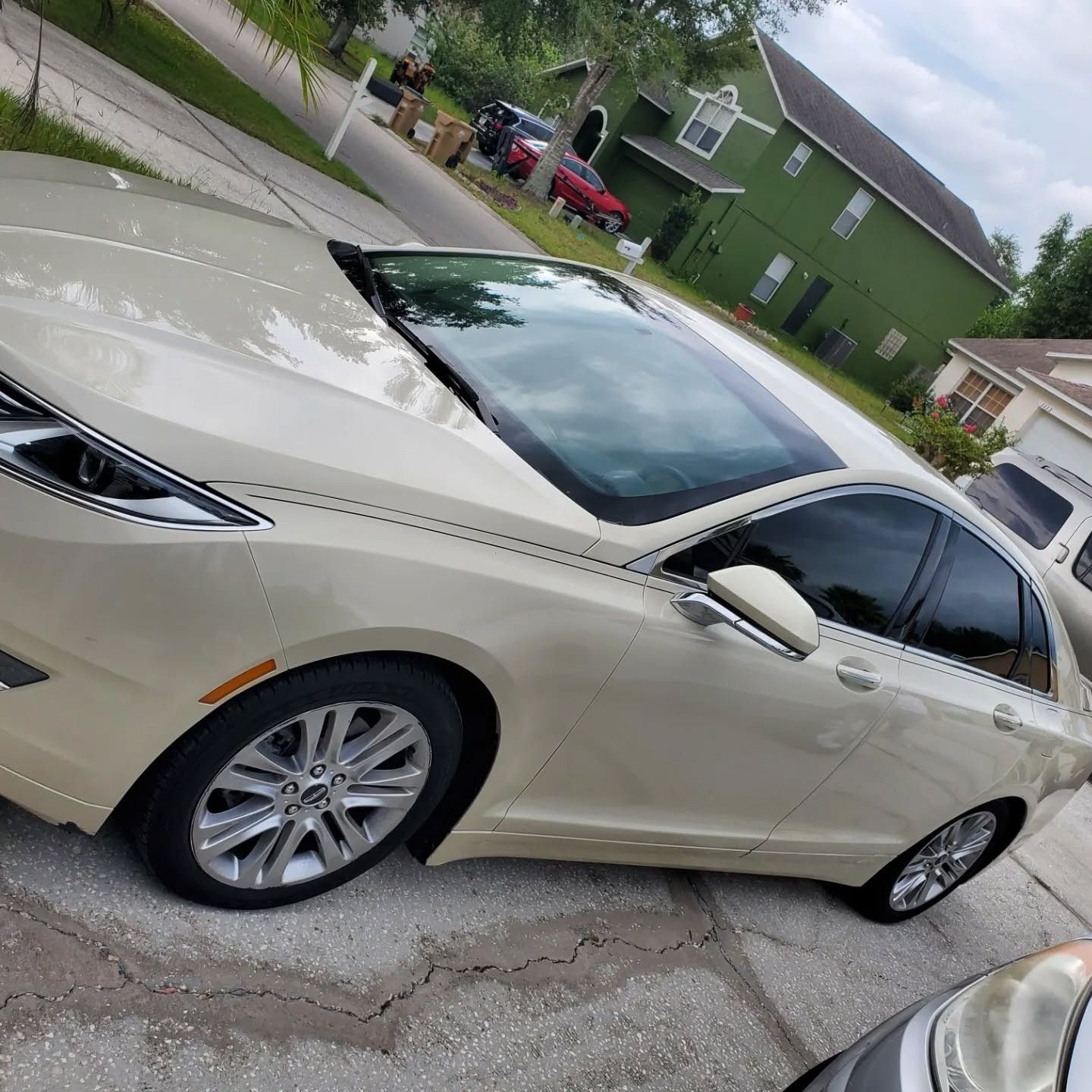 A white car is parked in front of a green house