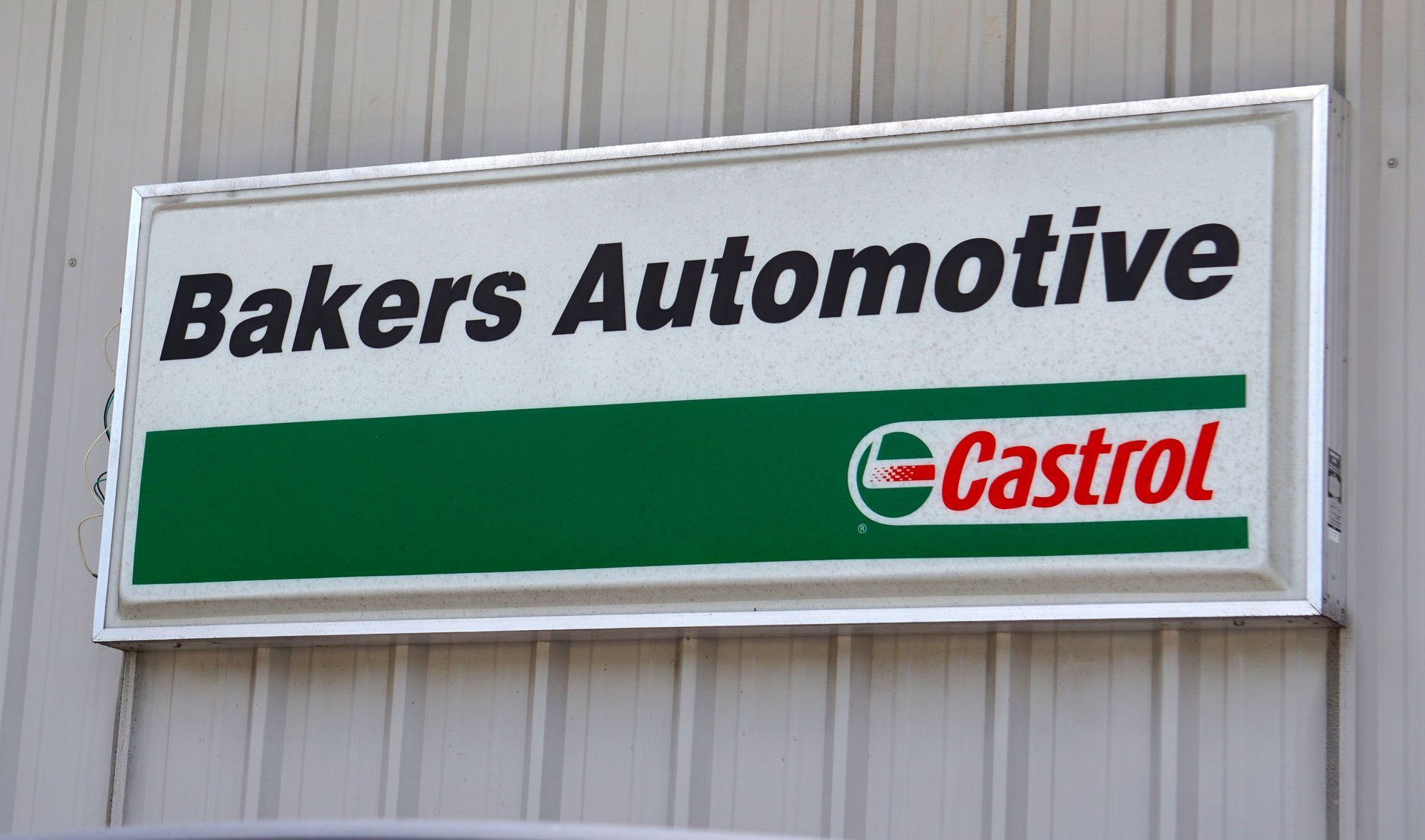 Sign for Baker's Automotive, white rectangle with business name above a green Castrol logo.