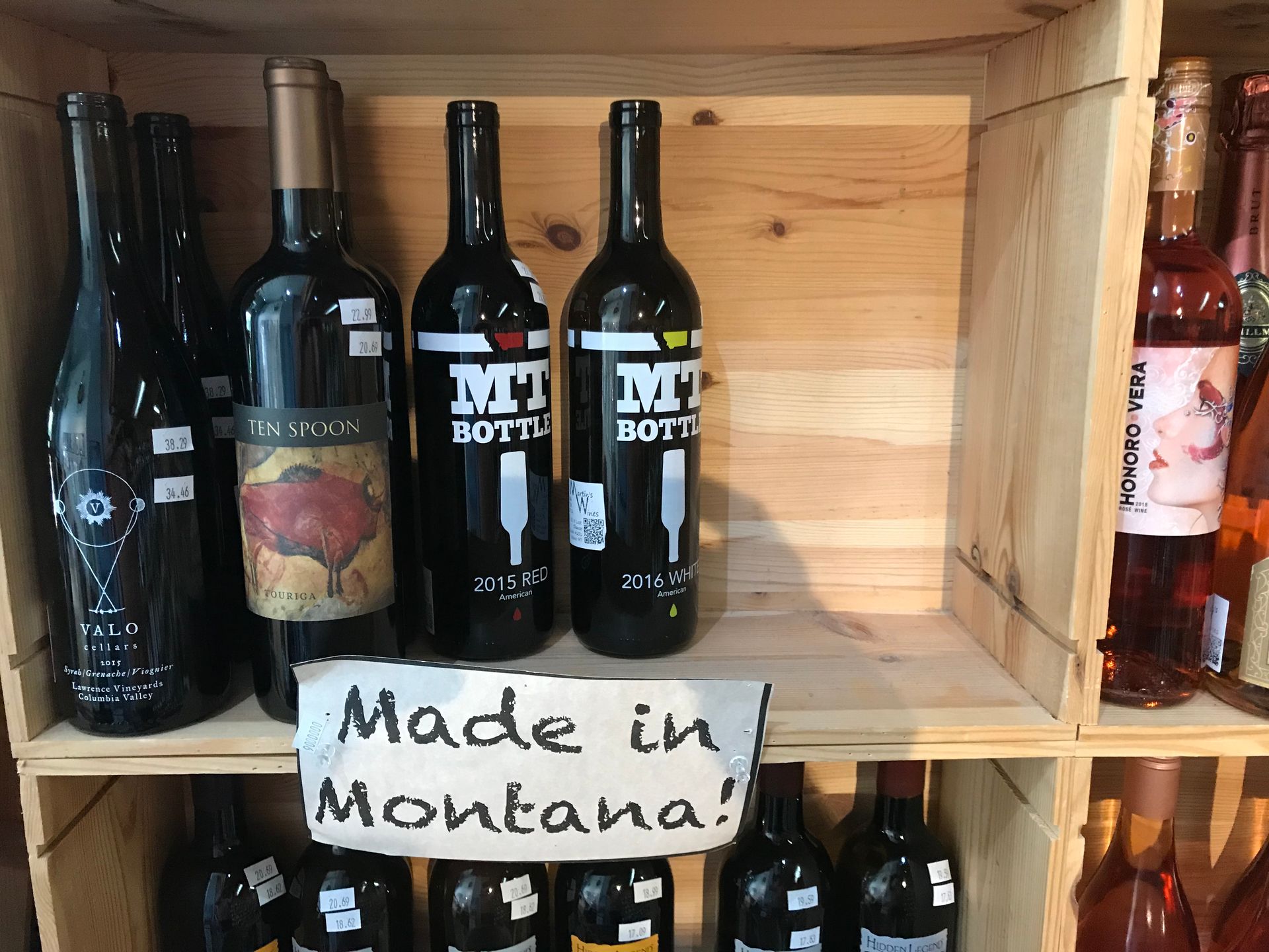 Bottles of wine are lined up on a shelf with a sign that says made in montana