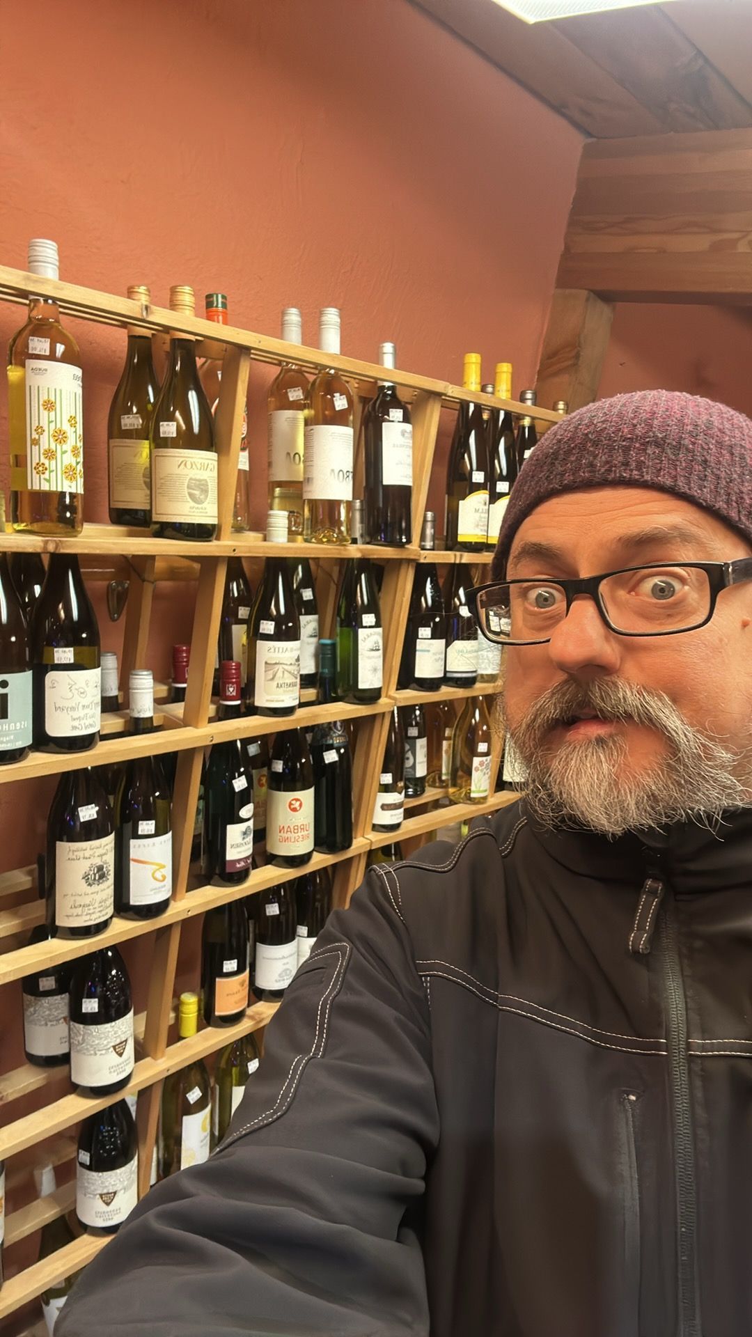 A man is standing in front of a wall of wine bottles.