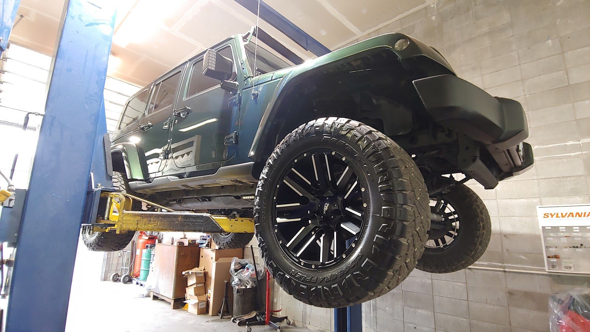 A green Jeep Wrangler lifted in a repair shop | Precision Axle Repair Ltd
