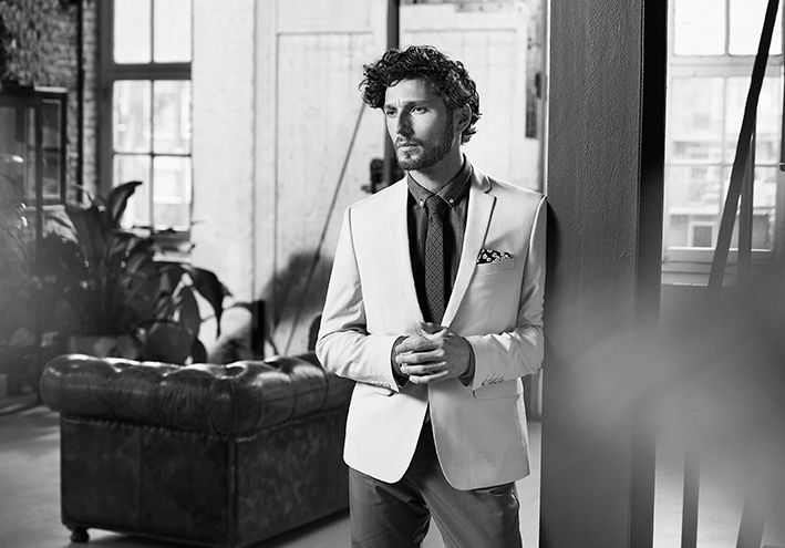 Man In A White Suit And Tie Is Standing In A Living Room — Siddha Hair Studio in Currajong, QLD