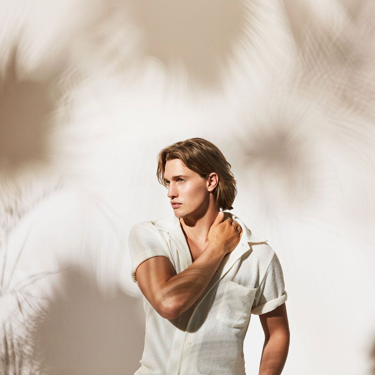 Man In A White Shirt Is Standing In Front Of A White Wall — Siddha Hair Studio in Currajong, QLD