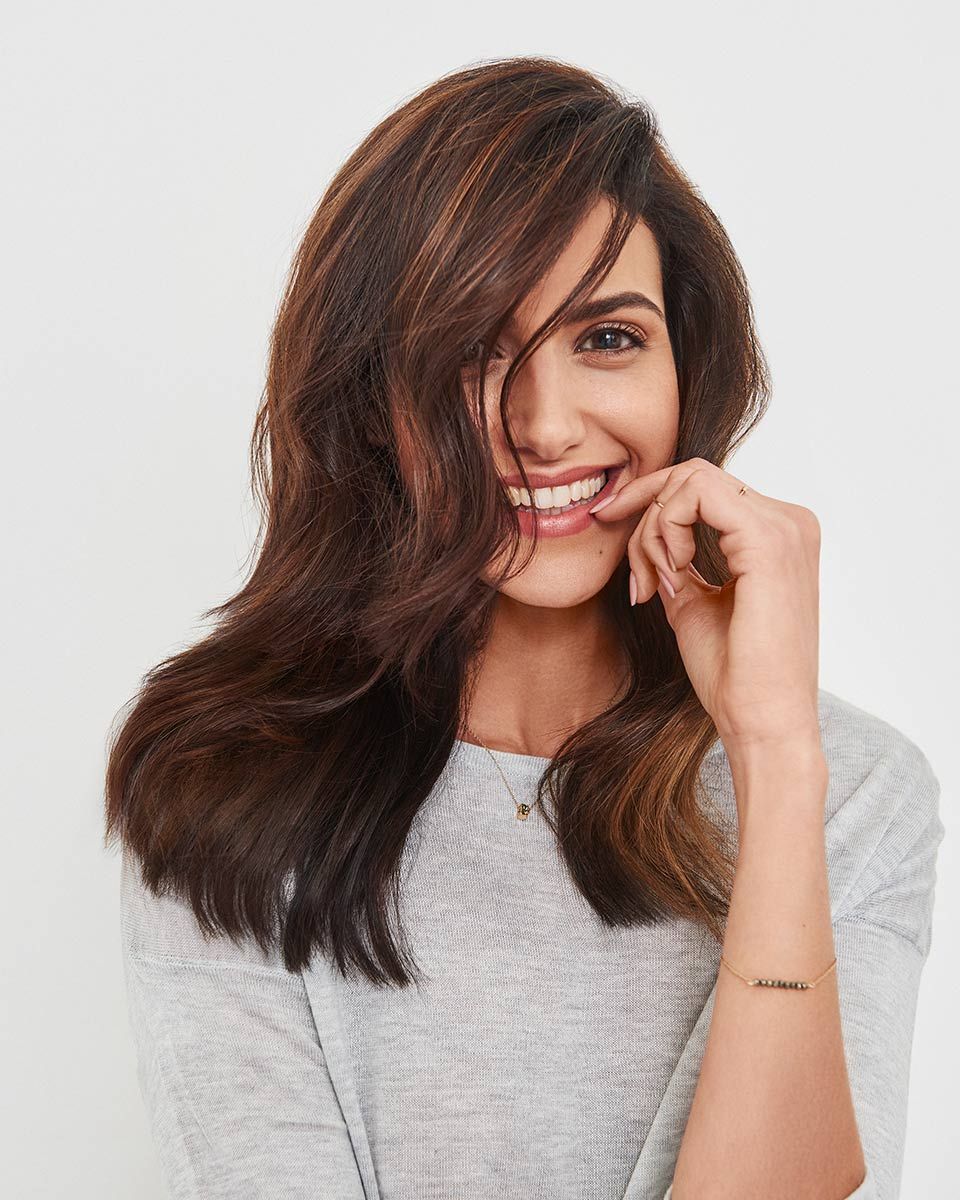 Woman With Long Brown Hair Is Wearing A Grey Sweater And Smiling — Siddha Hair Studio in Currajong, QLD