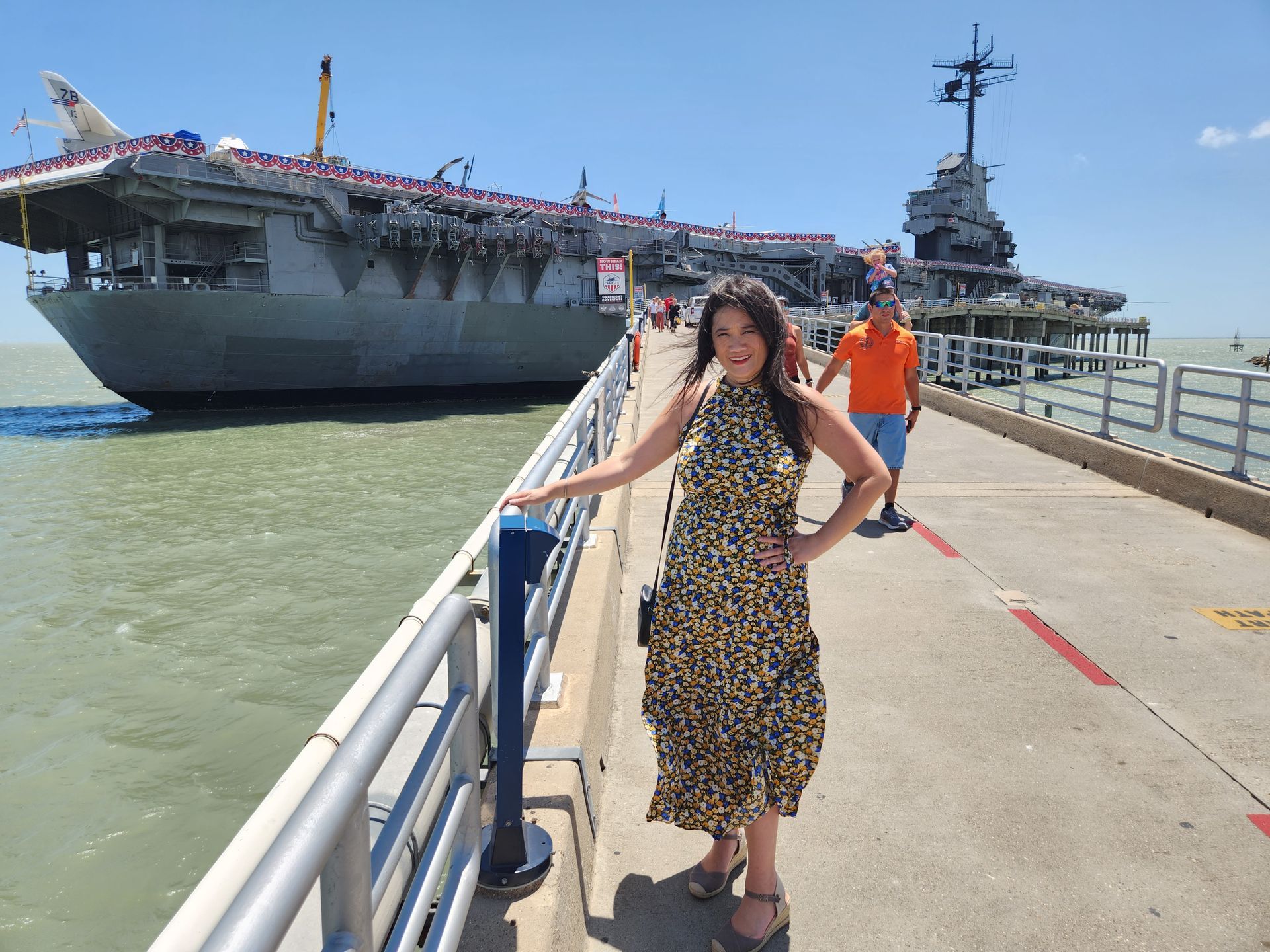 a woman is standing on a pier with a large ship in the background .