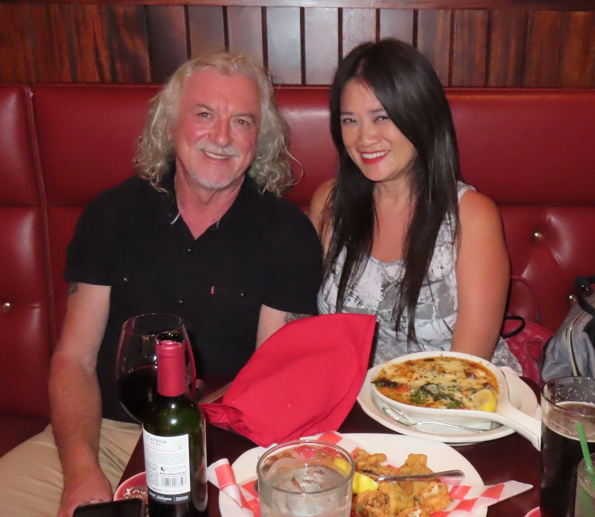 a man and a woman sit at a table with plates of food and a bottle of wine