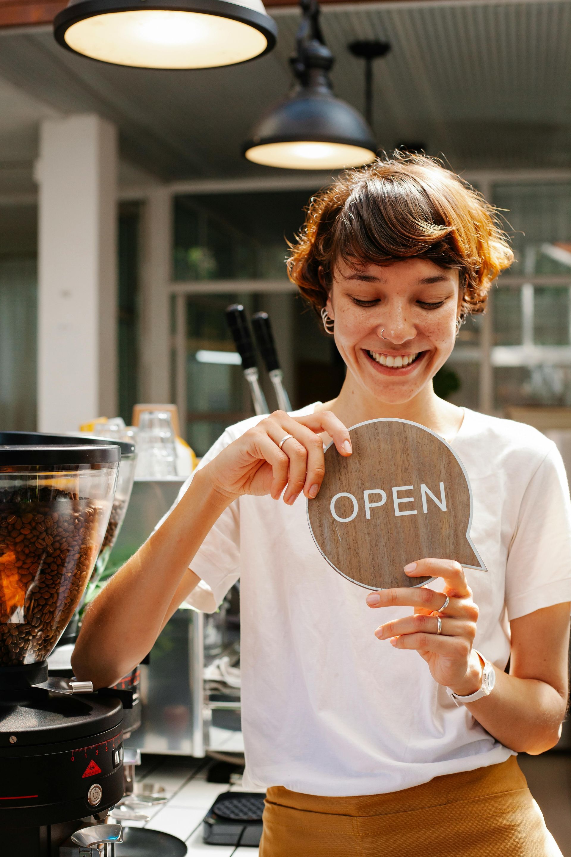 Barista smiling while writing “OPEN” on a coffee shop sign beside espresso equipment