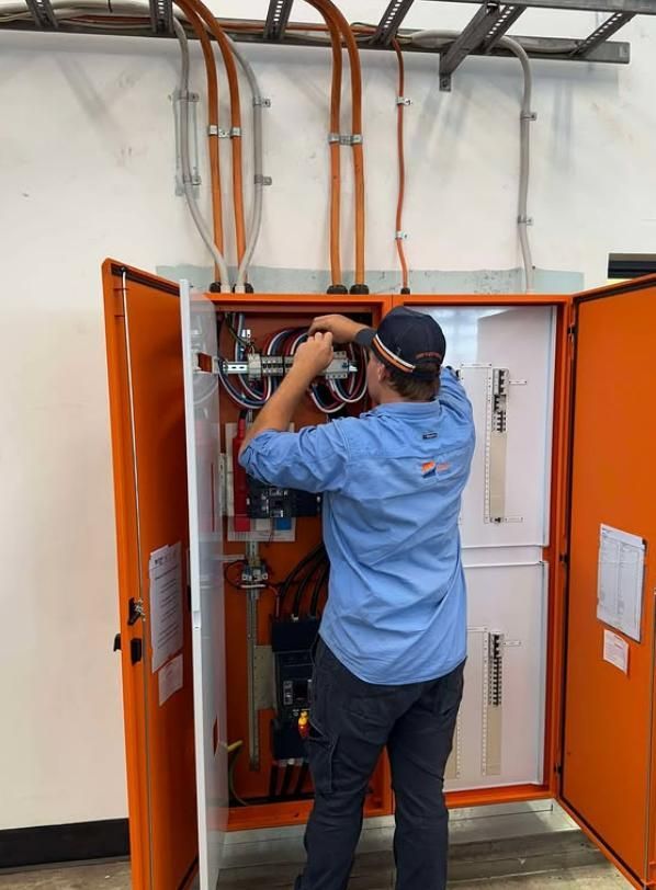 Electrician in Orange Cabinet, Wiring Circuits, Wearing Blue Shirt — DMP Electrical Contractors In Mandalong, NSW