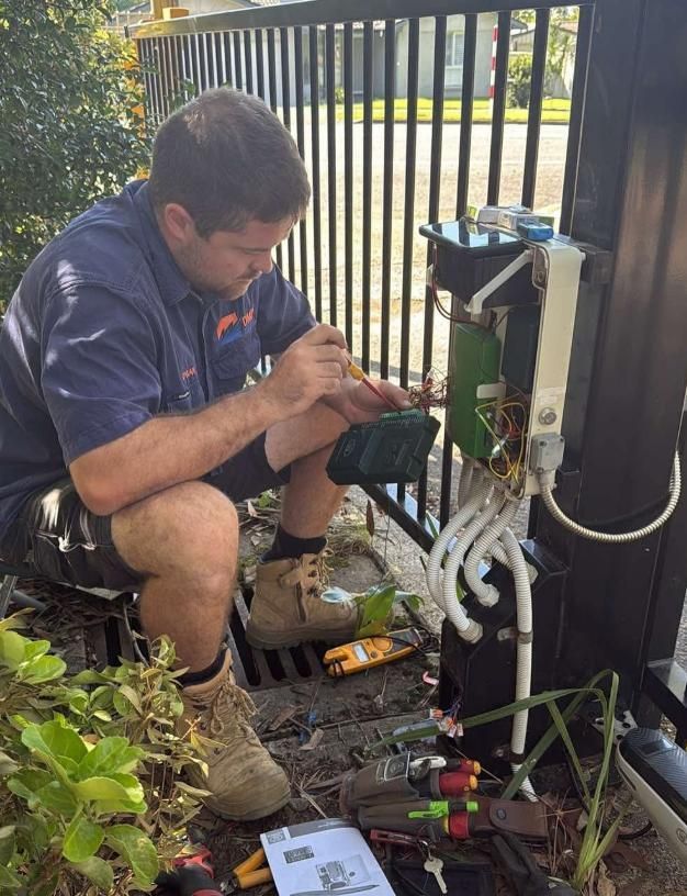 A Man in Work Clothes Fixing Gate Electronics Outdoors — DMP Electrical Contractors In Mandalong, NSW