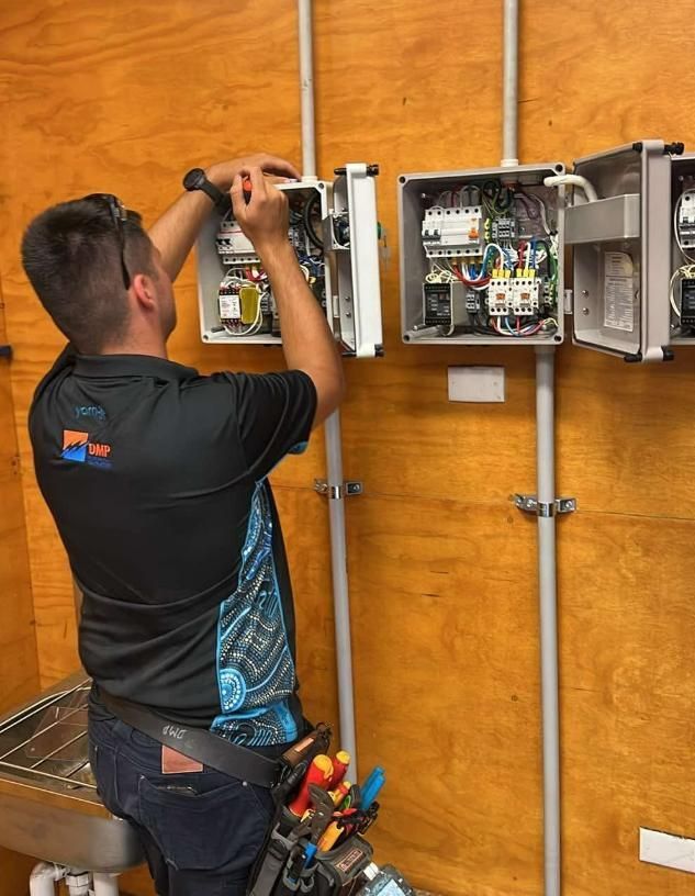 Electrician Working on Control Panels Mounted on a Wood Wall — DMP Electrical Contractors In Mandalong, NSW