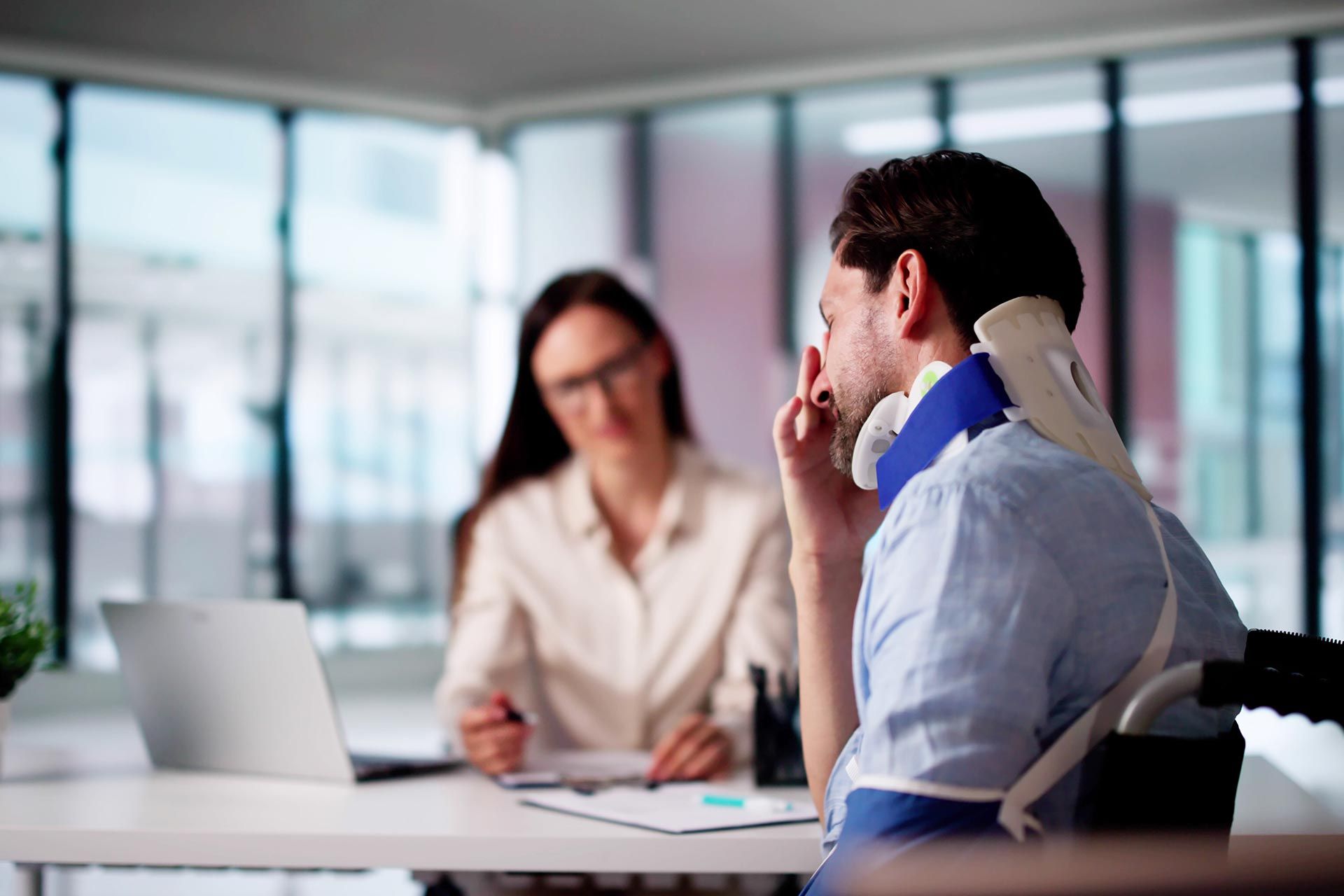 Injured man wearing neck brace consulting personal injury attorney in office.