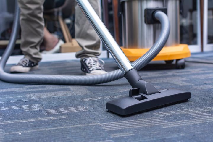 Person vacuuming a carpeted floor with a silver and black vacuum cleaner.