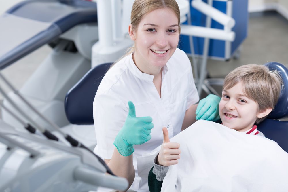 A Female Dentist is Giving a Thumbs Up to a Young Boy in a Dental Chair — Parap Family Dental in Parap, NT