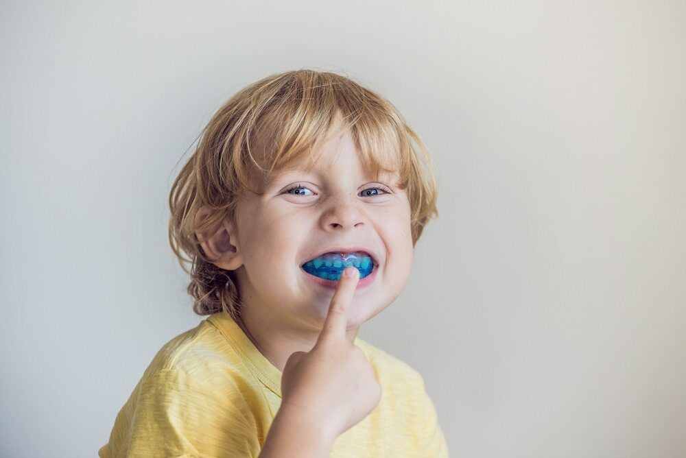 A Young Boy is Wearing a Blue Mouth Guard and Smiling — Parap Family Dental in Parap, NT