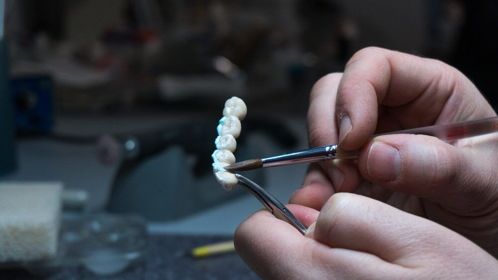 A Person is Working on a Dental Bridge With a Brush and Tweezers — Parap Family Dental in Parap, NT