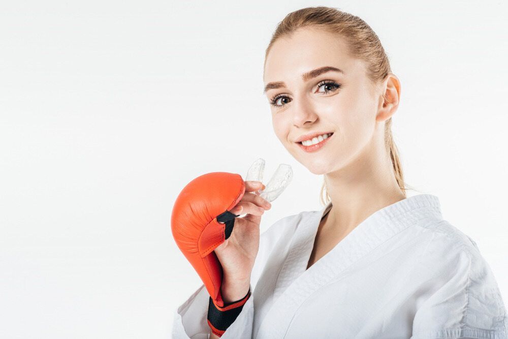 A Woman in a Karate Uniform is Wearing Boxing Gloves and Holding a Mouth Guard — Parap Family Dental in Parap, NT