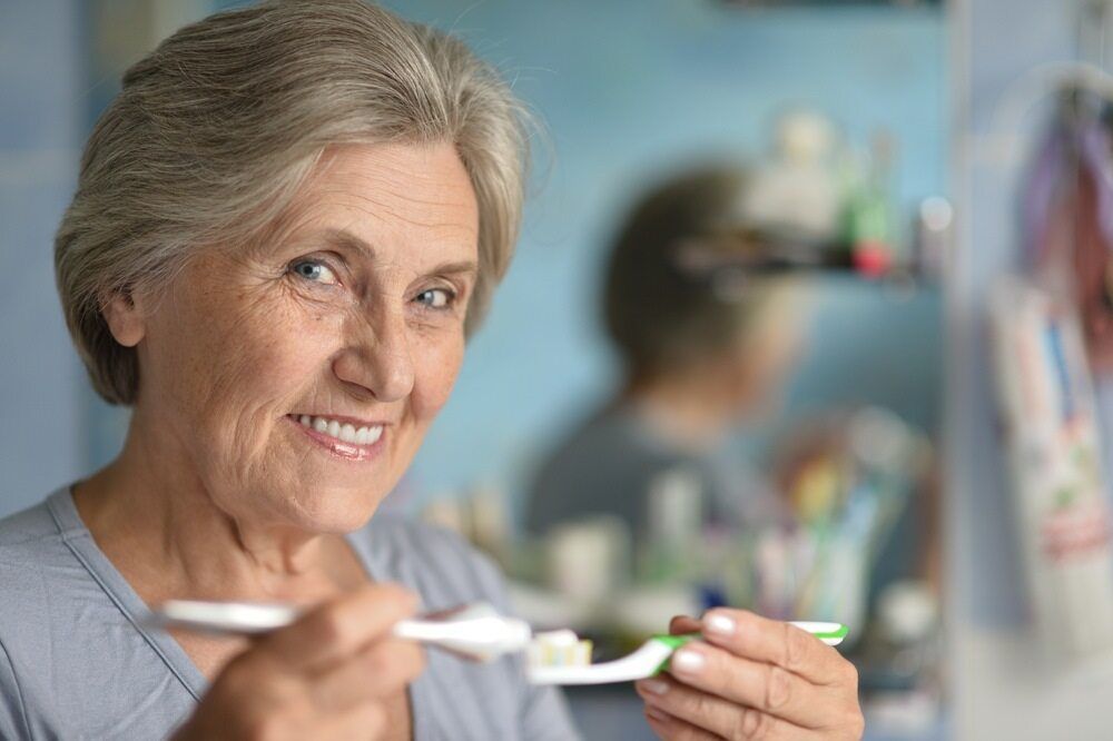 An Elderly Woman is Brushing Her Teeth in Front of a Mirror — Parap Family Dental in Parap, NT
