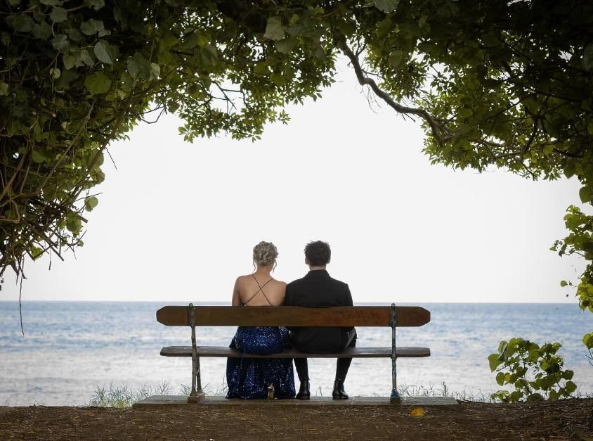 A Man And A Woman Are Sitting On A Bench Overlooking The Ocean — Jack West Photography In Kawungan, QLD