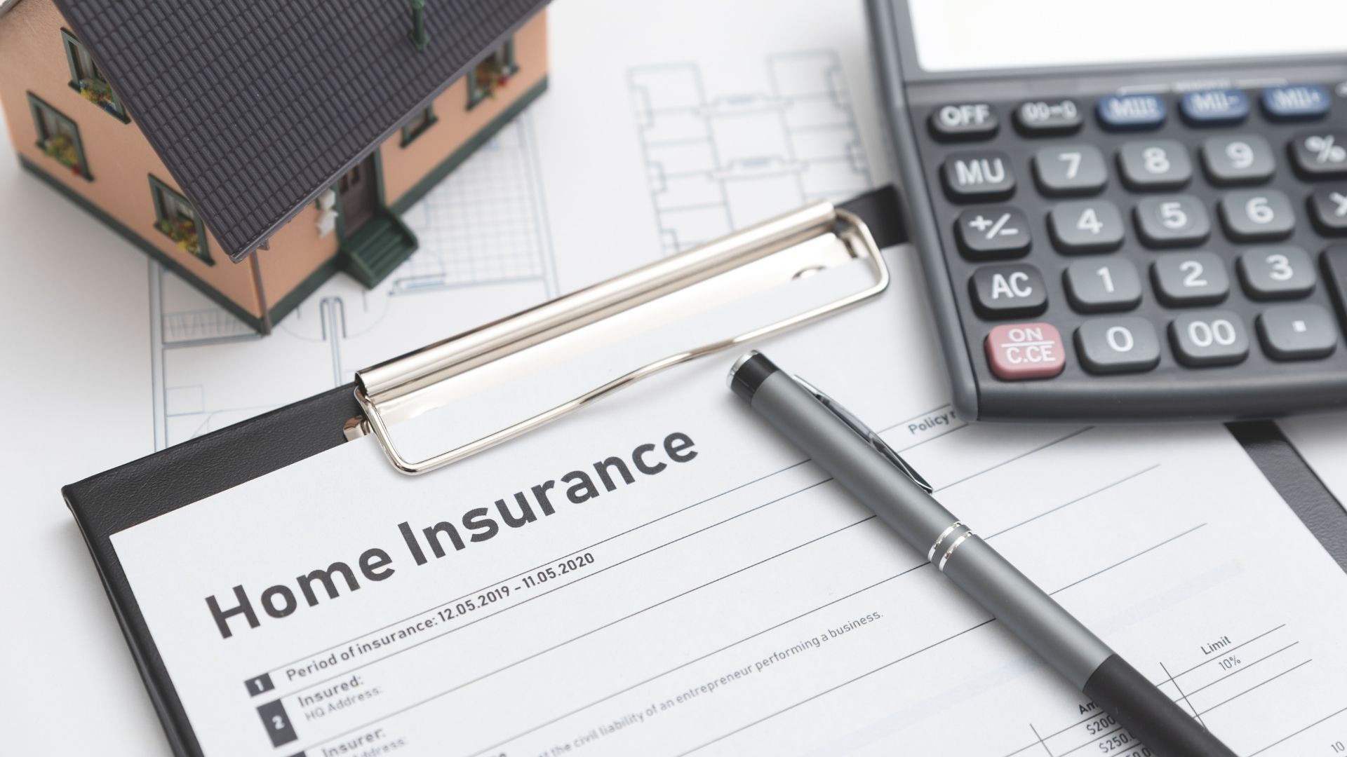 A clipboard with a pen , calculator and a model house on it.