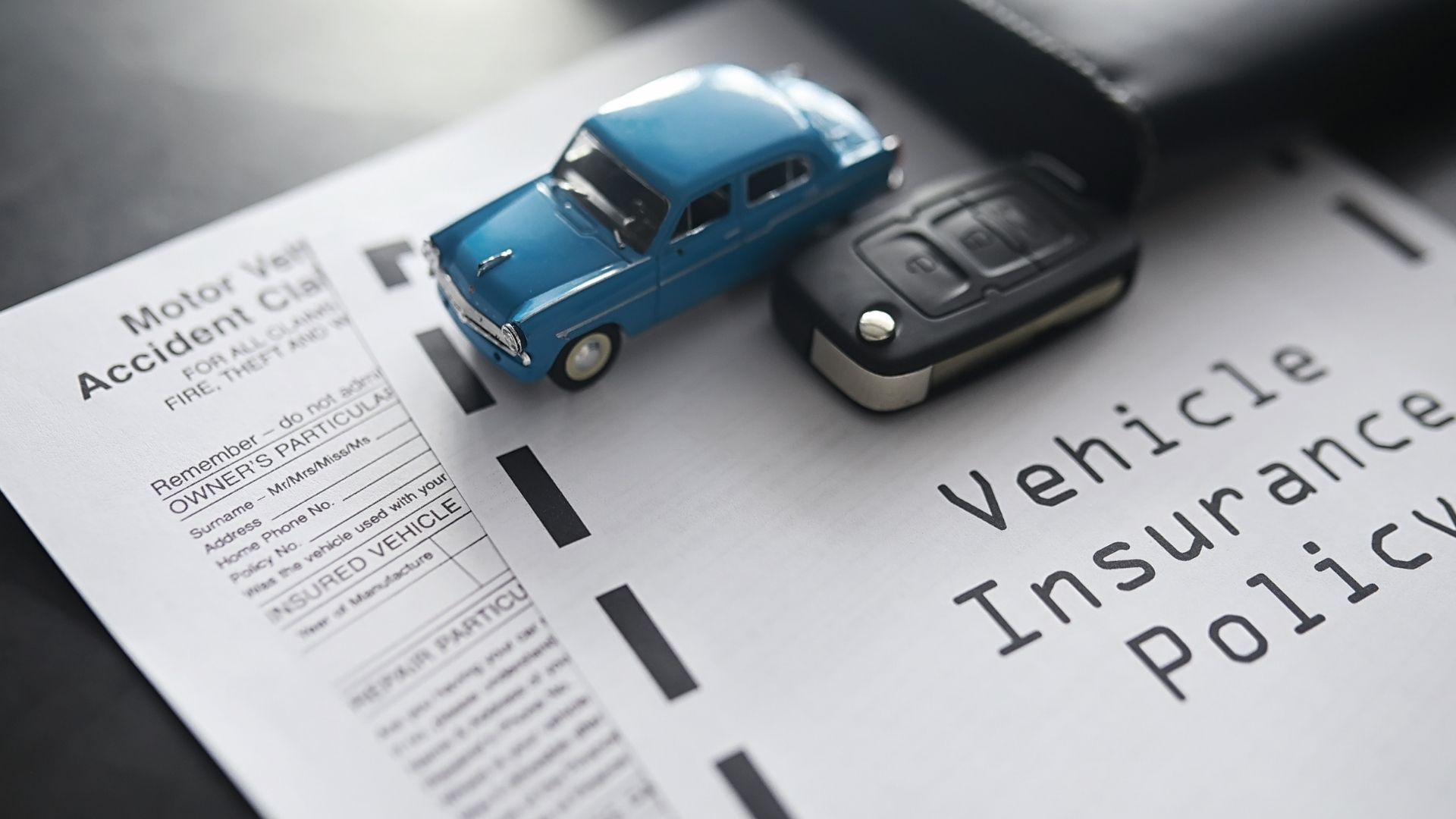 A blue toy car is sitting on top of a vehicle insurance policy.