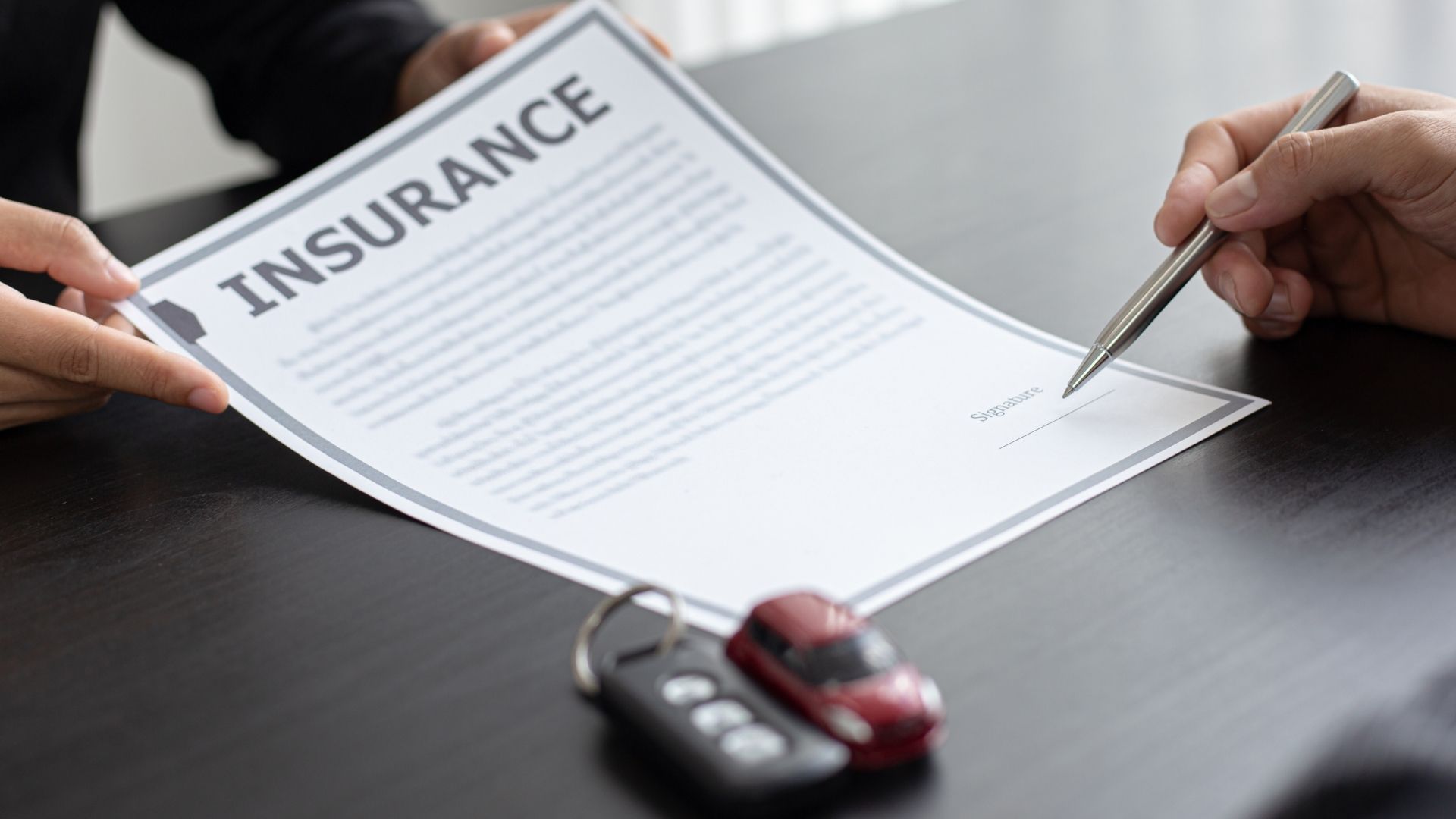 A person is signing a car insurance agreement with a pen.