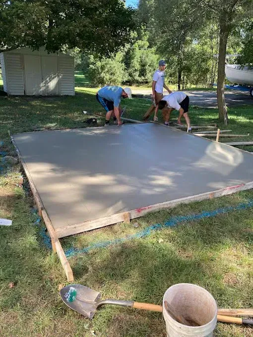 A group of men are working on a concrete floor in a yard.