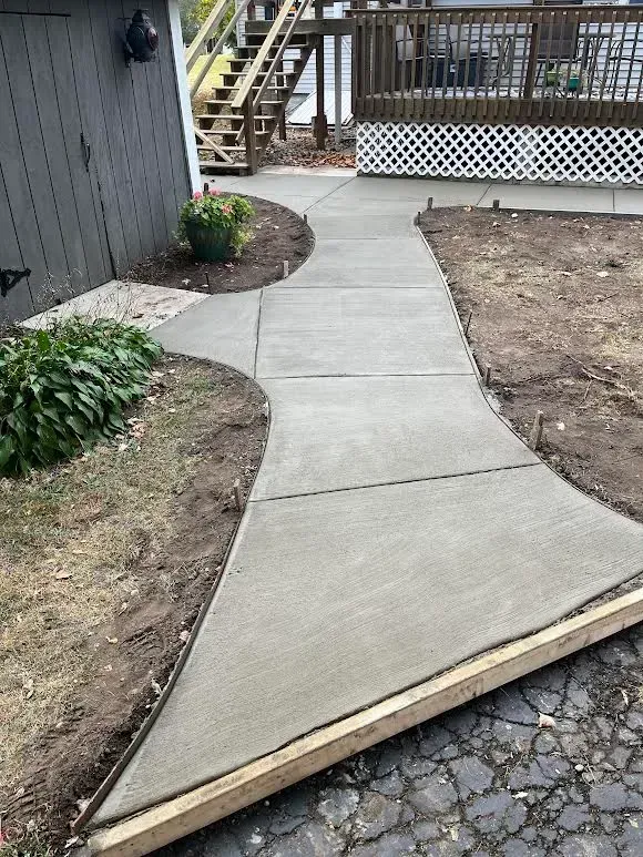 A concrete walkway is being built in the backyard of a house.