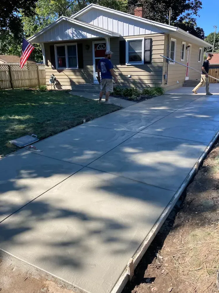 A man is standing on a concrete sidewalk in front of a house.