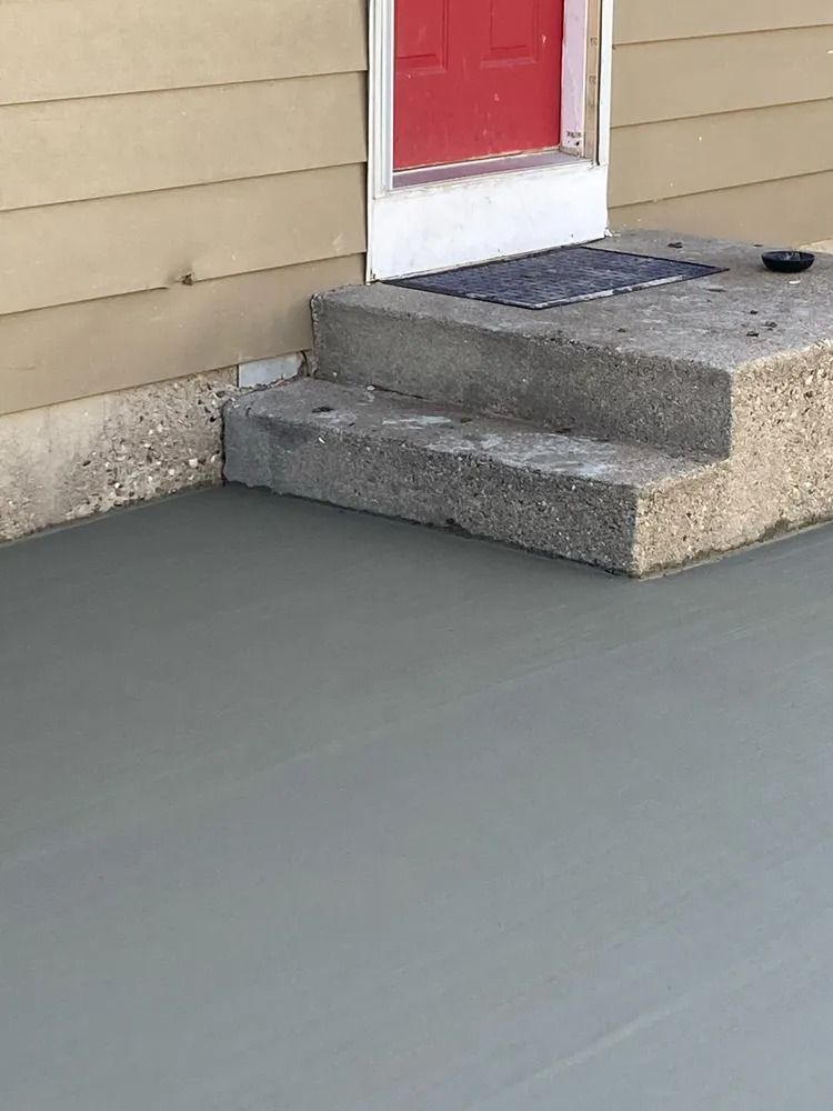 A concrete porch with stairs leading up to a red door.