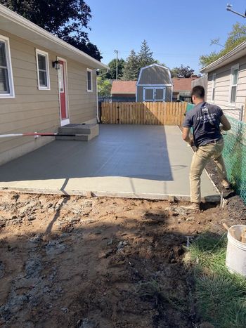A man is working on a concrete driveway in front of a house.
