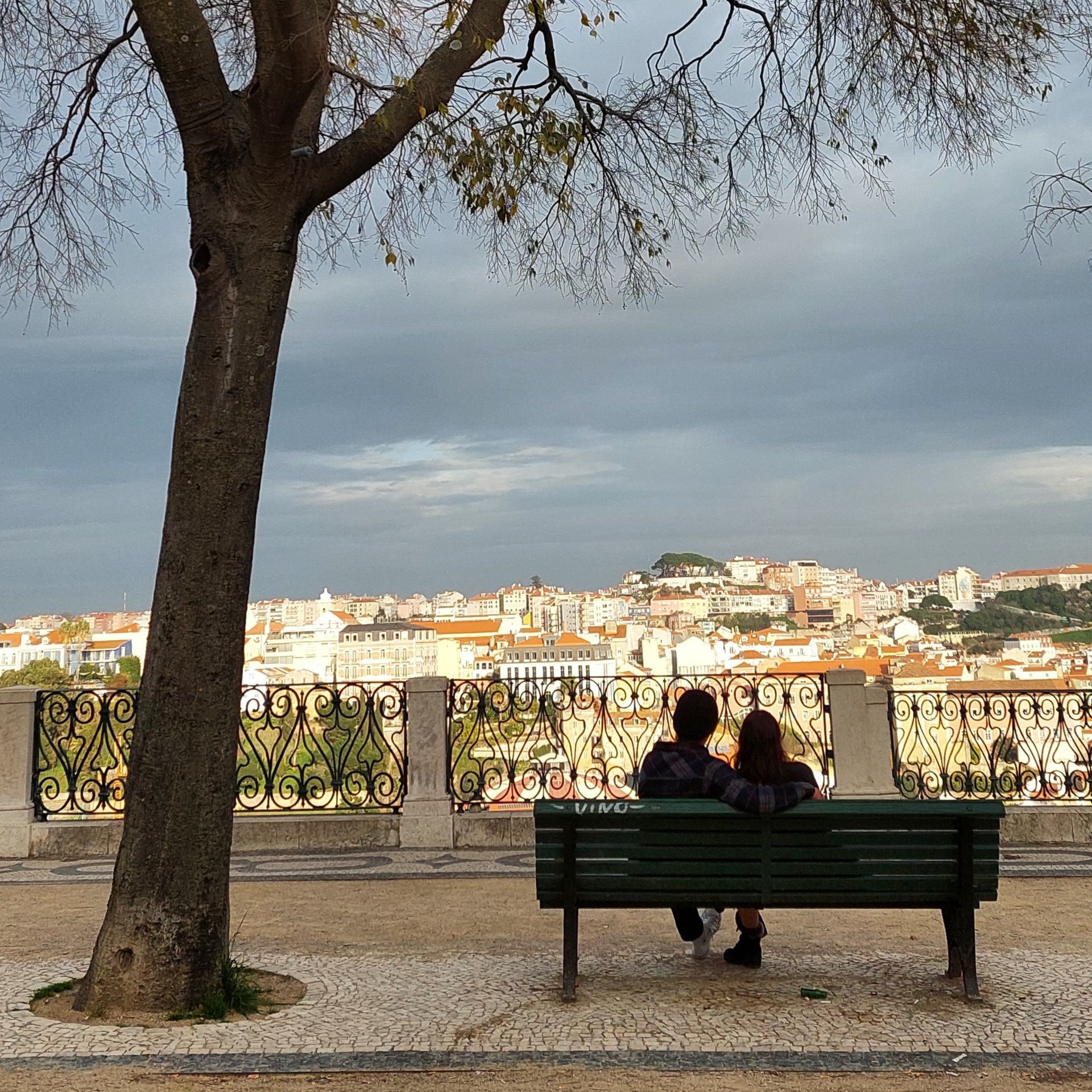 A quiet, intimate moment of a couple sitting on a bench, overlooking the most complete cityscape of Lisbon.