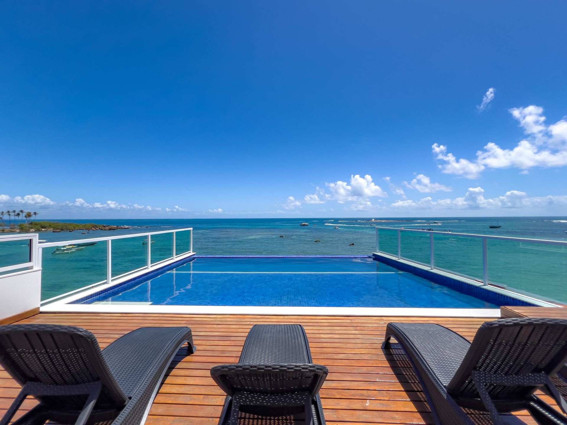 Uma cadeira de vime está sobre um deck de madeira ao lado de uma piscina com vista para o oceano.