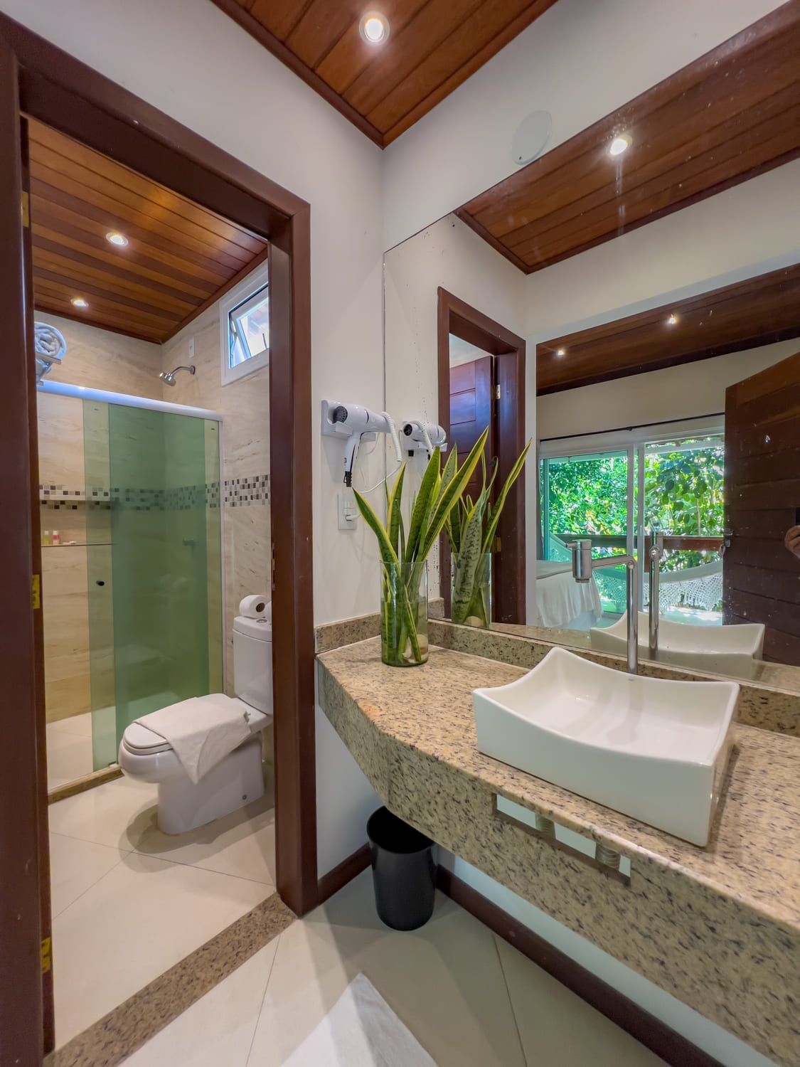 Um banheiro com vaso sanitário, pia, chuveiro e espelho.